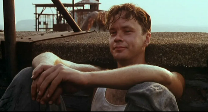 Character Andy Dufresne (Tim Robbins) sits tentatively against a brick wall 