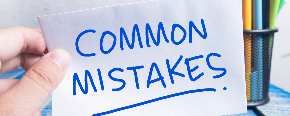 A finger holds a white paper with the words common mistakes written in blue marker