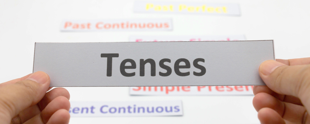 Hands holding a white paper with the words "tenses" written in black